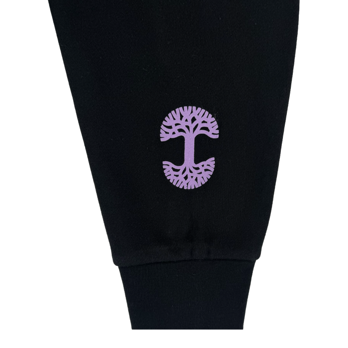 A close-up of a black pant leg shows a purple tree graphic with intricate branches and roots near the cuff. Pair it perfectly with the GSV Renowned Hoodie by GSV. The photo has a plain white background.