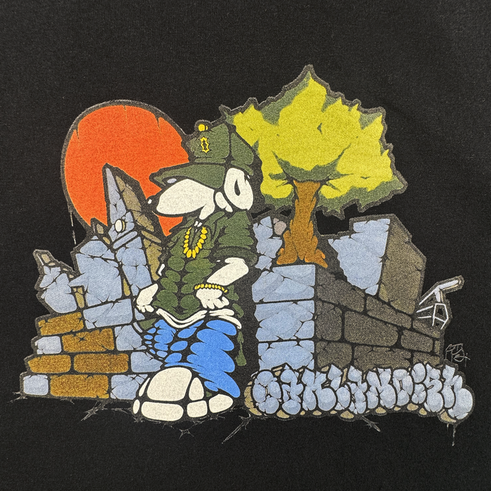 A cartoon dog in hip-hop gear leans on a graffiti stone wall, with a tree and red sun behind “Of Moundrock” text. This bold design stands out on the Oaklandish Highroller Tee, a men’s black, heavyweight cotton shirt.