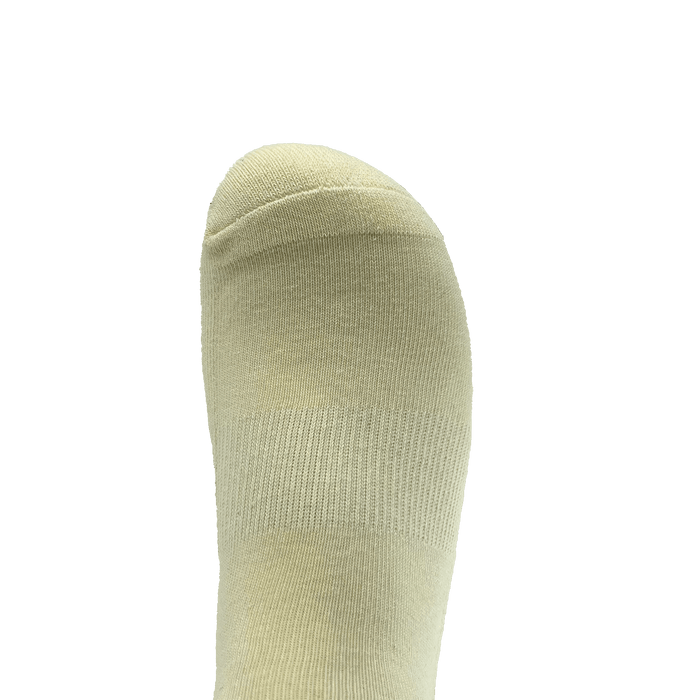 A close-up view of a foot wearing an Oaklandish Kanji Sock in beige, shown from above. The sock, available in adult sizes, covers the entire foot with subtle ribbing around the toe area and features a smooth texture. The background is green.