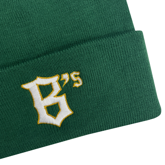 A close-up image of the Oakland Ballers Logo Beanie, a green knit hat with the letters "B's" embroidered on the fold to represent the Oakland Ballers professional baseball team. The text features a white, stylized font with a yellow outline. The beanie’s texture and stitching are clearly visible against the plain, light gray background.