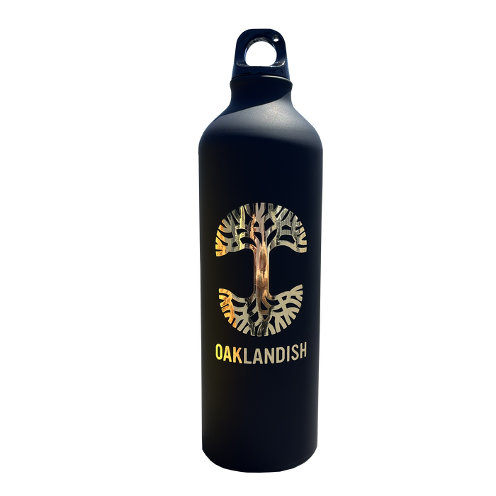 The Oaklandish Logo Aluminum Water Bottle by Oaklandish is crafted from single-wall aluminum and features a striking black exterior. The front showcases the iconic Oaklandish tree logo nestled within a circular "C" shape, along with "OAKLANDISH" boldly displayed beneath in uppercase white letters. It comes with a convenient looped handle cap for easy carrying, set against a plain white background.