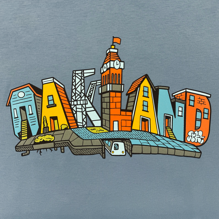 The Oaklandish Women's Blockletters Tee features "Oakland" spelled in illustrated, colorful buildings and landmarks—a clock tower as the "L" and an underground train—capturing the urban skyline on soft cotton.