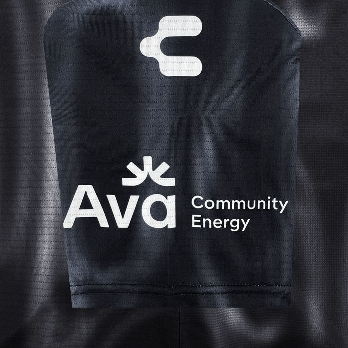 Close-up of black polyester fabric with a subtle dotted pattern, featuring bold white Oakland Soul logos and text, including the stylized "O" above "Ava Community Energy," all standing out clearly on the 2026 OAKLAND SOUL SC SPIRIT JERSEY.