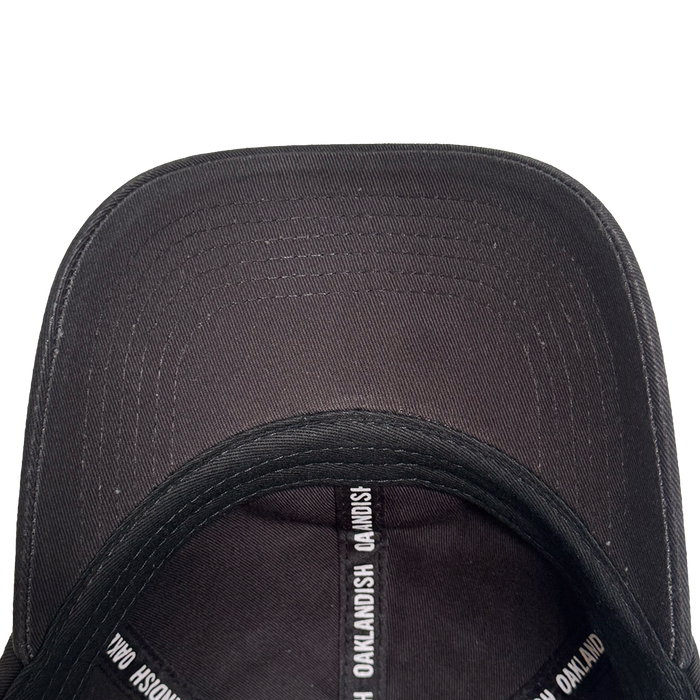 Top-down view of the inside of the AC Transit Dad Hat by Oaklandish. The inner seams feature repeating white "OAKLANDISH" text, celebrating East Bay pride. Its curved brim and stitching details stand out against a plain white background.