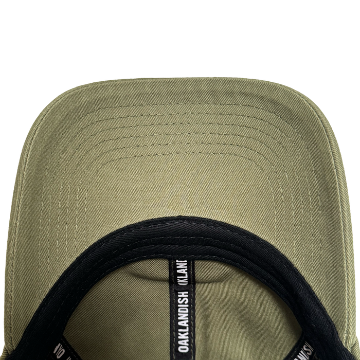 Close-up underside view of the olive green AC Transit Dad Hat brim with parallel stitching. A black sweatband features repeating white "Oaklandish" logo labels, celebrating East Bay style by Oaklandish.