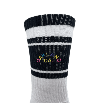 Detailed close-up of full-color OAKLAND CALIFORNIA wordmark on the side calf of a black and white crew sock.