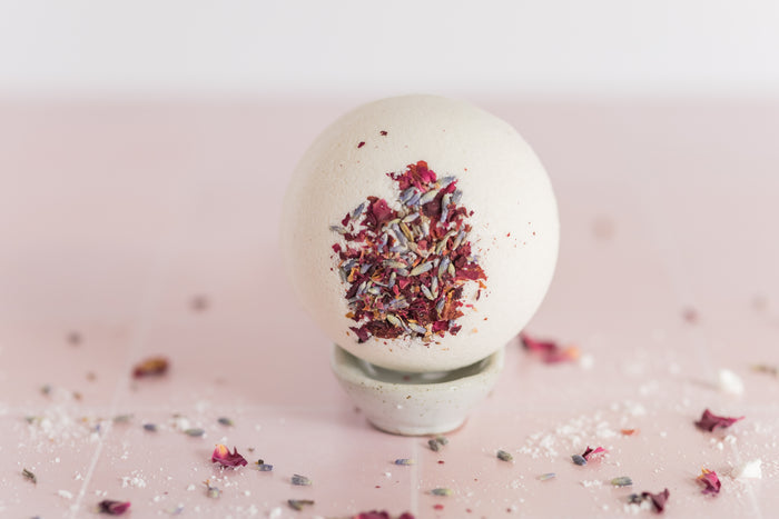 large bath bomb with dried flowers embedded in it with lavender buds and rose petals scattered around