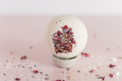 large bath bomb with dried flowers embedded in it with lavender buds and rose petals scattered around