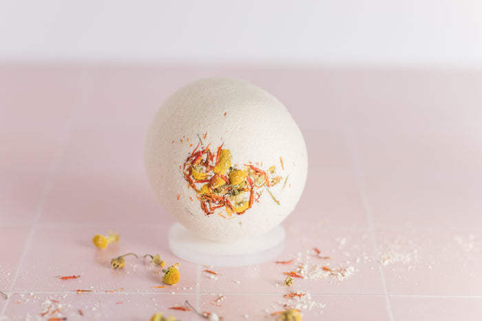 bath bomb on tile with dried chamomile buds and safflower petals scattered around it
