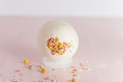 bath bomb on tile with dried chamomile buds and safflower petals scattered around it