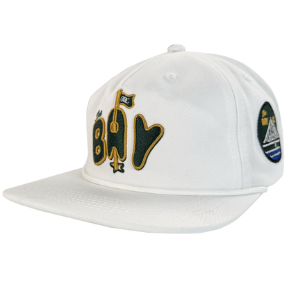 The Bay Area 5 Panel by DOC from Oaklandish is a white, unstructured baseball cap with stylized yellow and black "Bay" text and a flag graphic. Part of The Bay Collection, it features a flat brim, visible stitching, and an adjustable strap back.