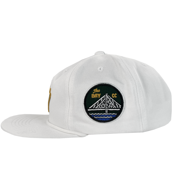 The Bay Area 5 Panel By DOC from Oaklandish is a white, unstructured strap back hat with a left-facing flat brim and a side embroidered patch showing a white bridge over blue water with "The Bay CC." Part of The Bay Collection.