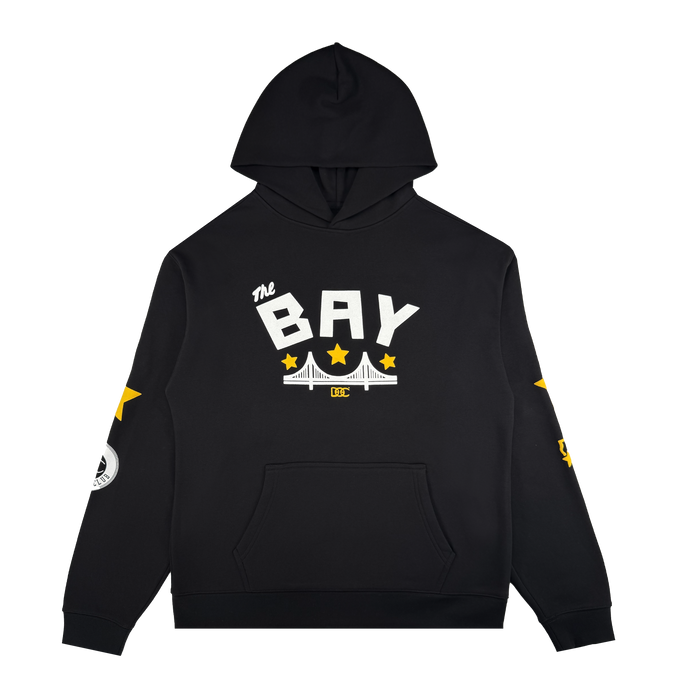 The Bay Bridge Hoodie By DOC V2 by Oaklandish is a black men’s fleece pullover with a front pouch pocket, “the BAY” in bold white above a bridge and yellow stars. Sleeve accents feature stars and graphics. Hood up; plain white background.