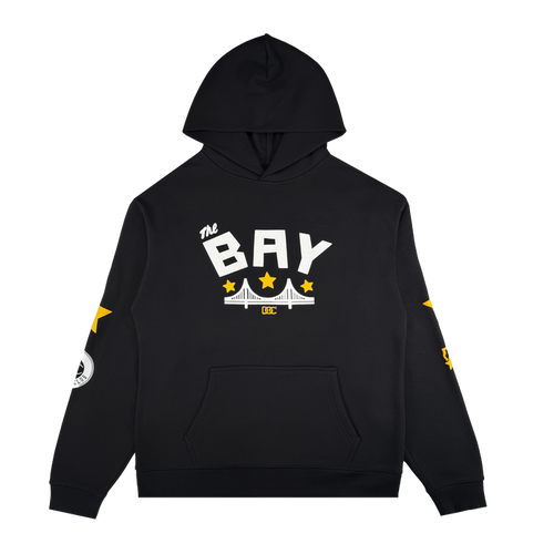The Bay Bridge Hoodie By DOC V2 by Oaklandish is a black men’s fleece pullover with a front pouch pocket, “the BAY” in bold white above a bridge and yellow stars. Sleeve accents feature stars and graphics. Hood up; plain white background.