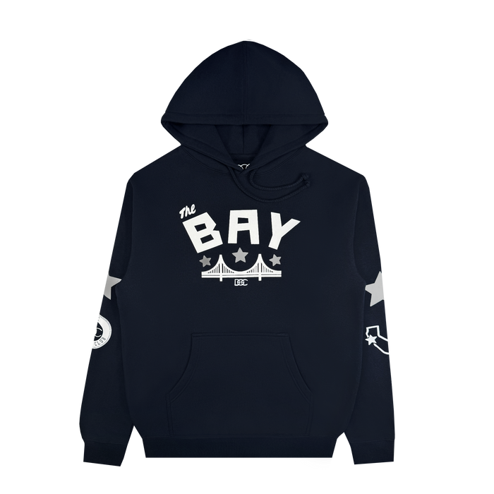 The Bay Bridge Hoodie by DOC, from brand Other, is a black pullover featuring “The BAY” in bold white text above a bridge graphic—an ode to Bay Area pride. White stars accent the sleeves, complemented by a circular emblem on the right sleeve and a curved arrow motif on the left. This stylish hoodie offers a front pocket and drawstring hood for added comfort and functionality.
