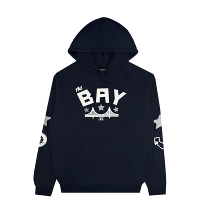 The Bay Bridge Hoodie by DOC, from brand Other, is a black pullover featuring “The BAY” in bold white text above a bridge graphic—an ode to Bay Area pride. White stars accent the sleeves, complemented by a circular emblem on the right sleeve and a curved arrow motif on the left. This stylish hoodie offers a front pocket and drawstring hood for added comfort and functionality.