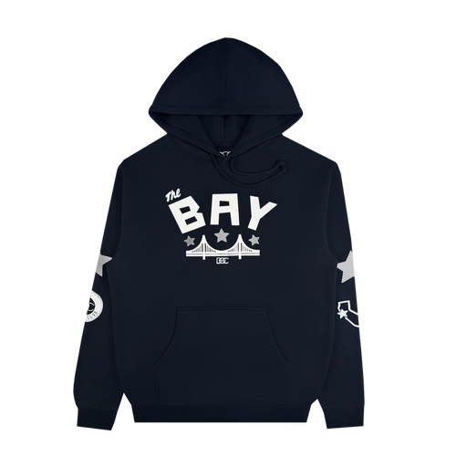 The Bay Bridge Hoodie by DOC, from brand Other, is a black pullover featuring “The BAY” in bold white text above a bridge graphic—an ode to Bay Area pride. White stars accent the sleeves, complemented by a circular emblem on the right sleeve and a curved arrow motif on the left. This stylish hoodie offers a front pocket and drawstring hood for added comfort and functionality.