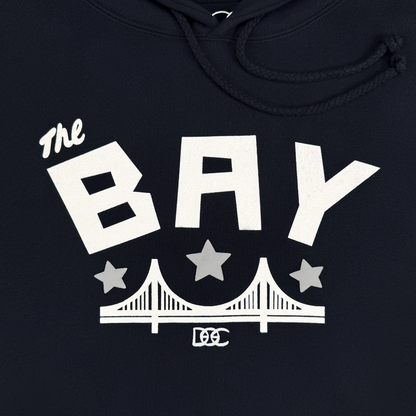 Sure! Here is your rewritten sentence using the provided product data: The Bay Bridge Hoodie by DOC from Other features white bold text “The BAY” above two stars and a stylized bridge graphic, with “DC” lettering below, all on a navy pullover hoodie with drawstrings—perfect for celebrating Bay Area pride.
