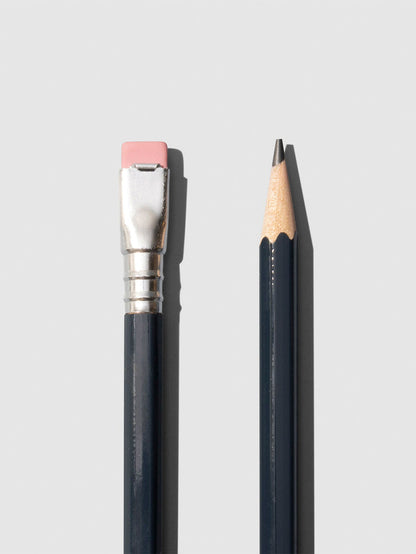 Closeup of dark grey wooden pencils displayed on a neutral background. One is shown eraser side up, the other point side up.