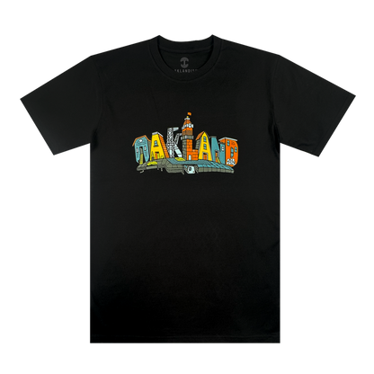 The Blockletters Tee by Oaklandish features "OAKLAND" in bold, colorful block letters with playful patterns. A small illustrated building above the "L" adds a touch of cityscape detail to this vibrant black t-shirt.