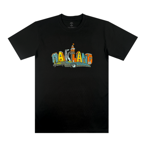 The Blockletters Tee by Oaklandish features "OAKLAND" in bold, colorful block letters with playful patterns. A small illustrated building above the "L" adds a touch of cityscape detail to this vibrant black t-shirt.
