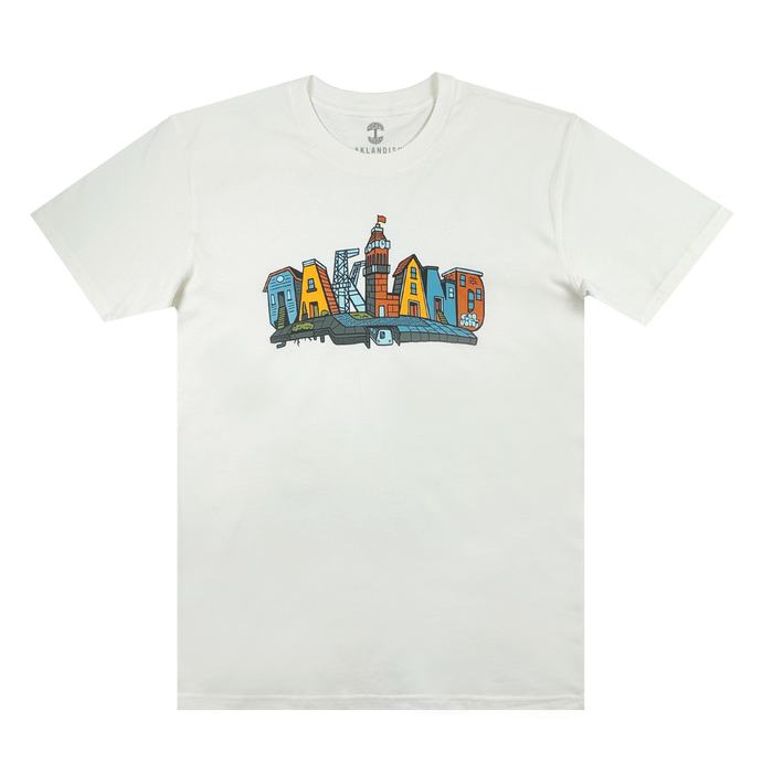 The Blockletters Tee by Oaklandish showcases “OAKLAND” in bold, colorful cityscape letters above a blue skyline, celebrating local landmarks with a vibrant urban design.