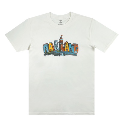 The Blockletters Tee by Oaklandish showcases “OAKLAND” in bold, colorful cityscape letters above a blue skyline, celebrating local landmarks with a vibrant urban design.
