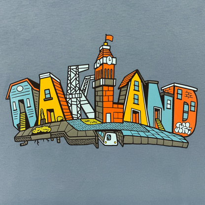 The Oaklandish Blockletters Tee features "OAKLAND" illustrated as colorful, stylized buildings—including houses, a clock tower, and a train—forming an imaginative city skyline on a plain gray background.
