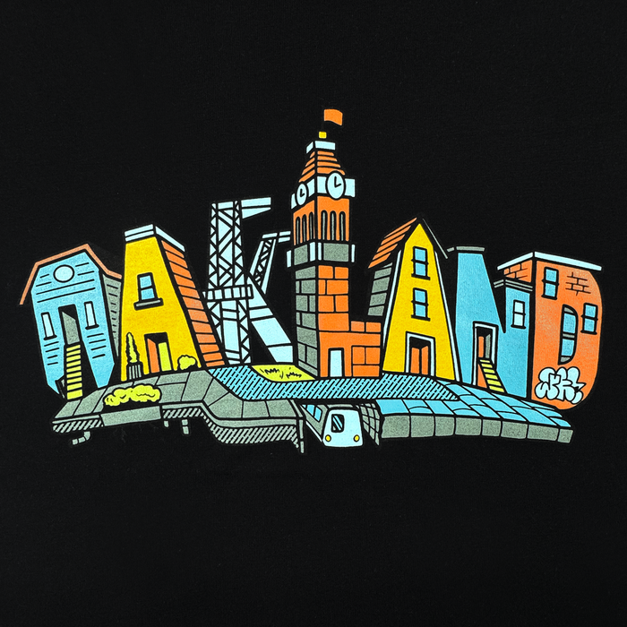 The Oaklandish Blockletters Tee features a vibrant cityscape spelling “Oakland” in unique building shapes, with a clock tower "L" and subway below, accented by graffiti—capturing the lively skyline against a black background.
