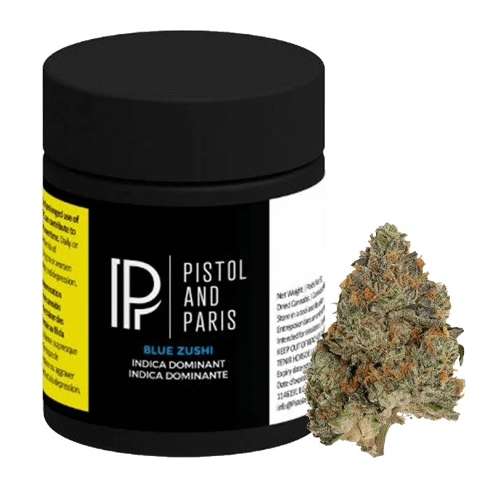Front three-quarter view of a black Pistol and Paris Blue Zushi jar with label details visible, shown beside a single green and orange cannabis bud.