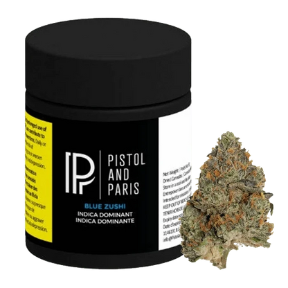 Front three-quarter view of a black Pistol and Paris Blue Zushi jar with label details visible, shown beside a single green and orange cannabis bud.