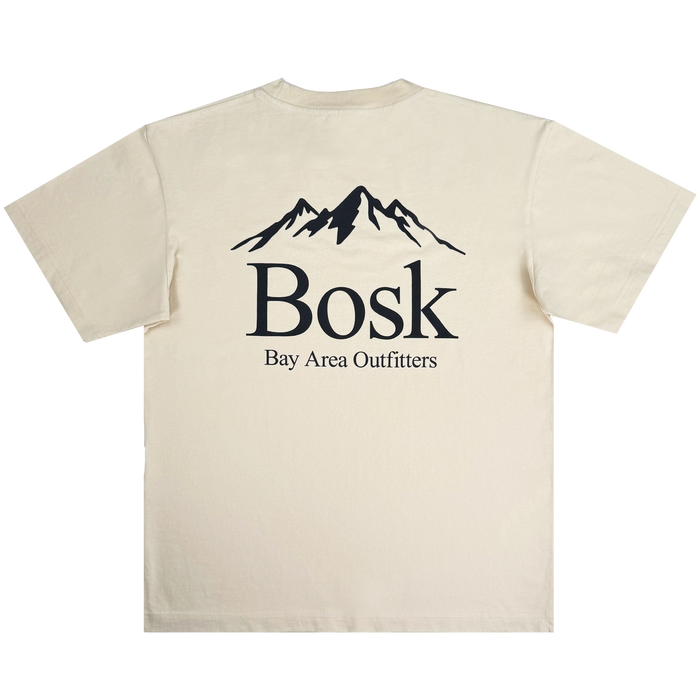 The Other brand Bosk Outdoors Tee is a beige, short-sleeve oversized fit t-shirt made from heavyweight cotton in men’s sizing. A bold black graphic decorates the back, featuring a mountain silhouette above the large “Bosk” text and smaller “Bay Area Outfitters” lettering beneath. The shirt is displayed laid flat on a white background.