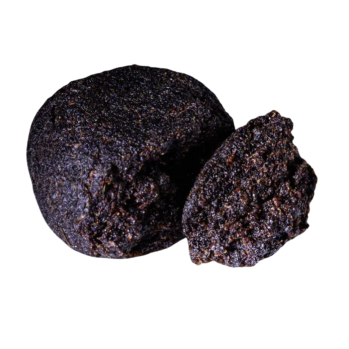 Close-up front view of a dark, crumbly ball and a halved piece of Bubble Yum Hash showing its granular, glistening texture.