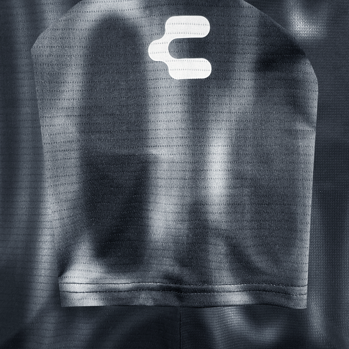 Close-up of the dark, textured fabric from the Custom 2026 Oakland Soul SC Spirit Jersey by Oakland Soul, featuring a large pocket and a white abstract logo near the top. Soft lighting highlights the mesh-like pattern and signature brand style.