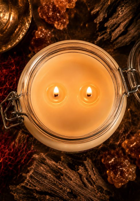 Amber & oud jar candle in clear glass with two lit wicks inside metal clasp lid