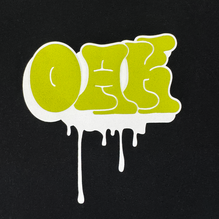 The Oaklandish Graff OAK Tee features "OAK" in bold, bright green graffiti letters with a dripping white outline on a solid black, 100% cotton classic fit.