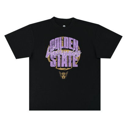 The GSV Fade Away Tee by GSV is a black, 100% cotton classic fit t-shirt featuring bold, distressed “Golden State Valkyries” lettering in purple and white. Beneath the text, a stylized golden Valkyrie face with a winged helmet is printed. The shirt is displayed flat on a white background.