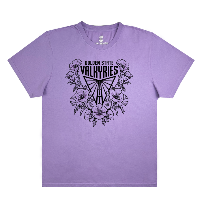The GSV Poppies Tee by GSV is a lavender garment-dyed, 100% cotton t-shirt featuring black “Golden State Valkyries” text above a stylized Valkyrie helmet surrounded by illustrated poppy flowers and leaves. This short-sleeve shirt has no additional designs or patterns.