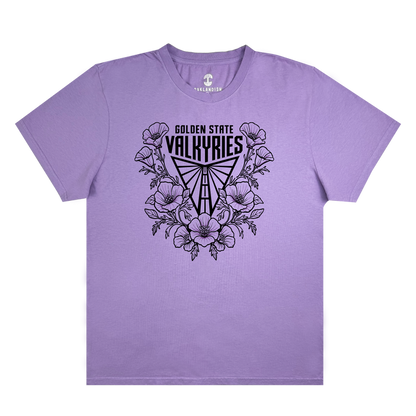 The GSV Poppies Tee by GSV is a lavender garment-dyed, 100% cotton t-shirt featuring black “Golden State Valkyries” text above a stylized Valkyrie helmet surrounded by illustrated poppy flowers and leaves. This short-sleeve shirt has no additional designs or patterns.