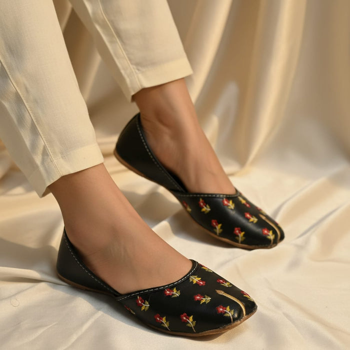 Black flats with floral pattern worn by a person on a beige fabric background