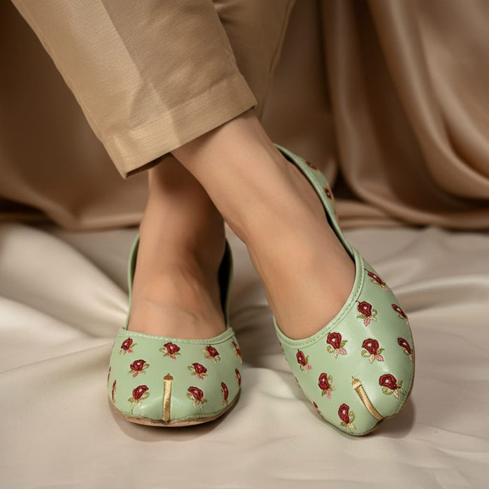 Green floral embroidered shoes worn with beige pants on a neutral background
