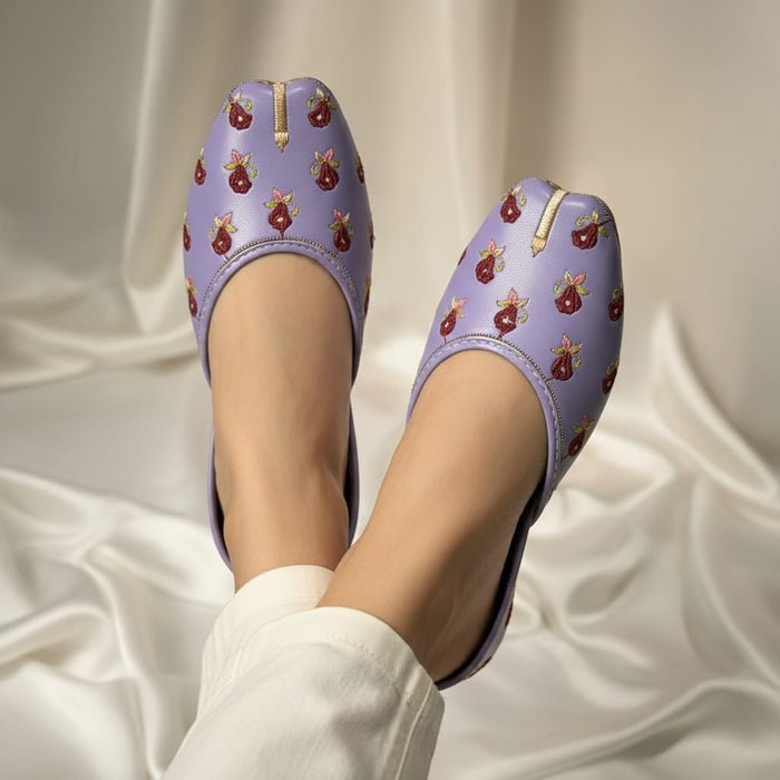 Purple shoes with floral patterns worn by a person on a white fabric background