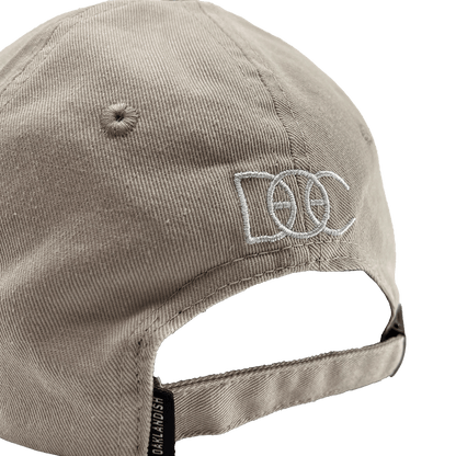 Angled back view of khaki Oakland Dad Hat designed by Dustin O. Canalin white embroidered DOC wordmark, adjustable strapback, and small Oaklandish wordmark tag.