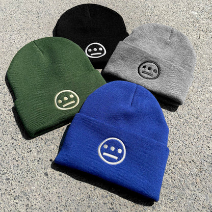 Four Hiero Classic Cuff Beanies from Hieroglyphics are laid out on a speckled gray surface. The headwear comes in black, gray, blue, and green. Each beanie features a minimalist face logo stitched in white thread at the center front, reminiscent of modern hieroglyphics.
