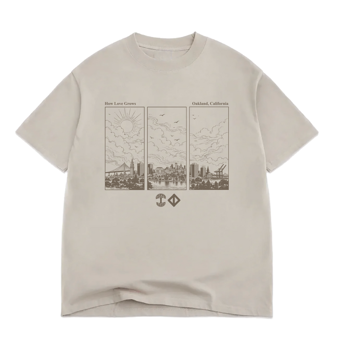 Beige 100% cotton Jwalt X Tidal Tee by Oaklandish in a classic fit, featuring a brown triptych line drawing of Oakland, California’s skyline with clouds, sun, birds, and cranes. The text above reads “How Love Grows” and “Oakland, California,” with two small geometric icons below the illustration.
