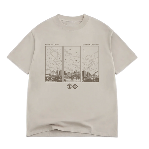 Beige 100% cotton Jwalt X Tidal Tee by Oaklandish in a classic fit, featuring a brown triptych line drawing of Oakland, California’s skyline with clouds, sun, birds, and cranes. The text above reads “How Love Grows” and “Oakland, California,” with two small geometric icons below the illustration.