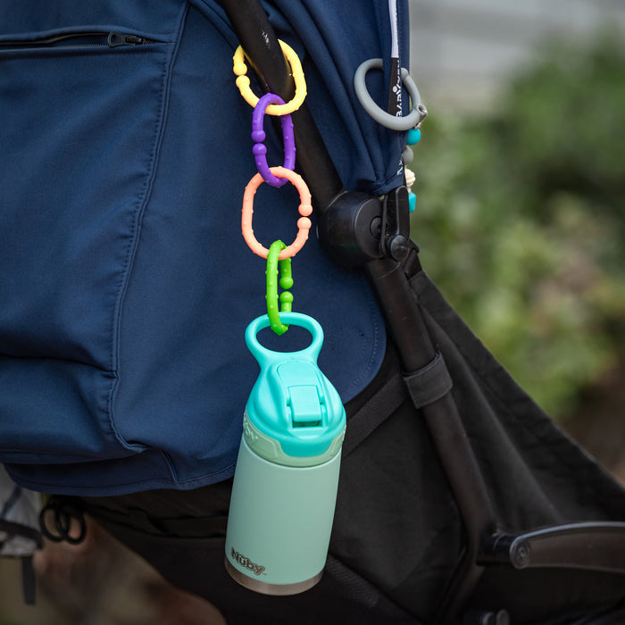 A mint green water bottle hangs from a stroller using Nuby Linkables Teething Toys - Primary Colors - 18 pack attached to the handle. The dark blue and black stroller stands out against a blurred green background.