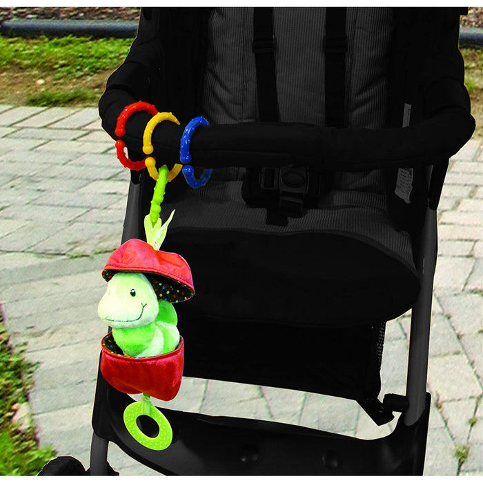 A stroller with a plush green turtle sensory toy is attached to the handlebar using Nuby Linkables Teething Toys in primary colors (18 pack); the stroller is outdoors on a paved path with grass in the background.