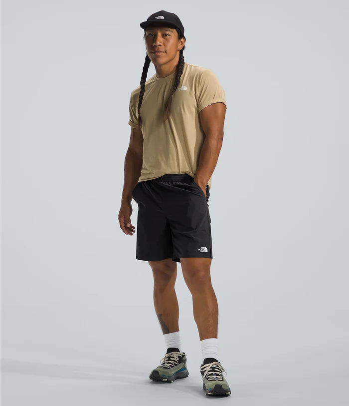 Person wearing a beige t-shirt, black shorts, and a cap on a light gray background