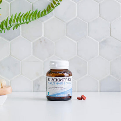 Blackmores Nails, Hair & Skin supplement bottle on a white surface with a hexagonal tile background.